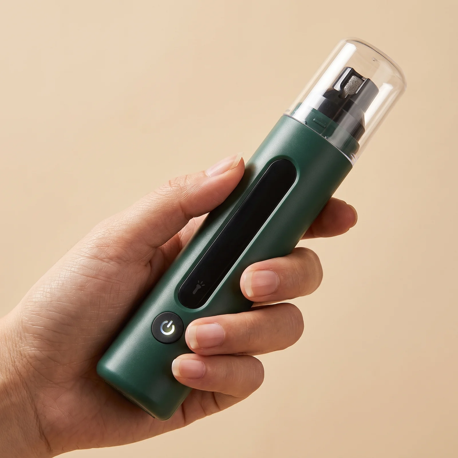 Hand holding the deep green grinder, showing its size, the button and the guard cap